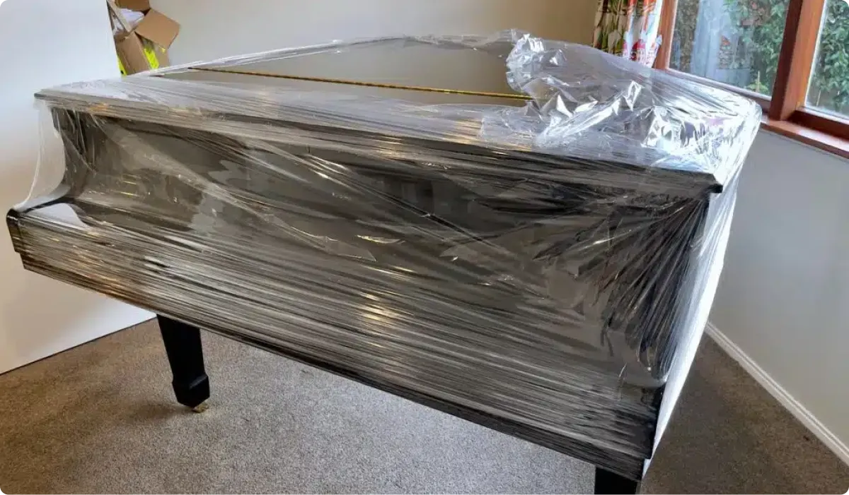 Professional piano movers preparing safe transport of black grand piano wrapped in plastic for moving